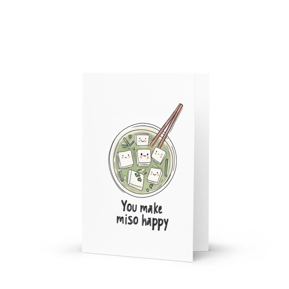 Whimsical illustration of a cute miso bowl filled with smiling tofu cubes, featuring the pun 'You make miso happy' on a bright white background, perfect for a quirky Valentine's Day greeting card.