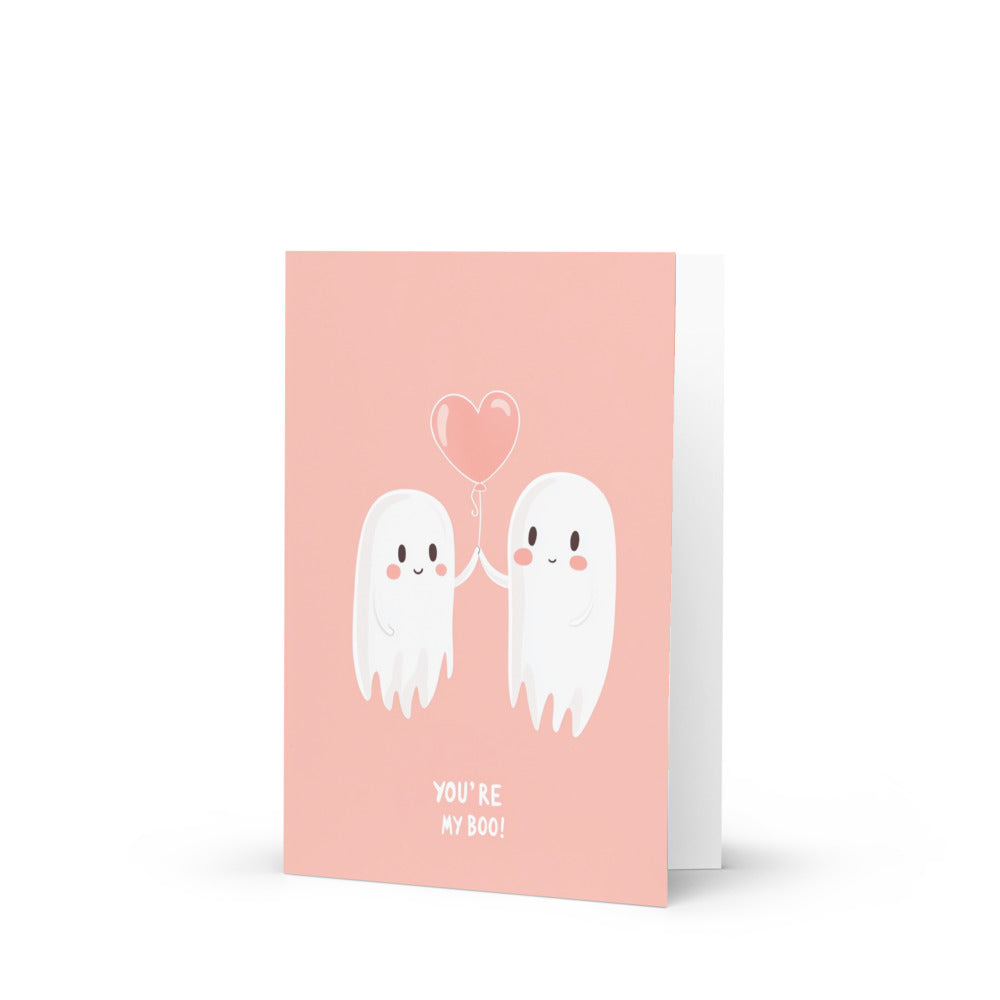 Adorable greeting card design featuring a cute ghost couple holding hands with a heart-shaped balloon, perfect for Halloween and romantic occasions, showcasing kawaii style illustration on a pastel pink background.